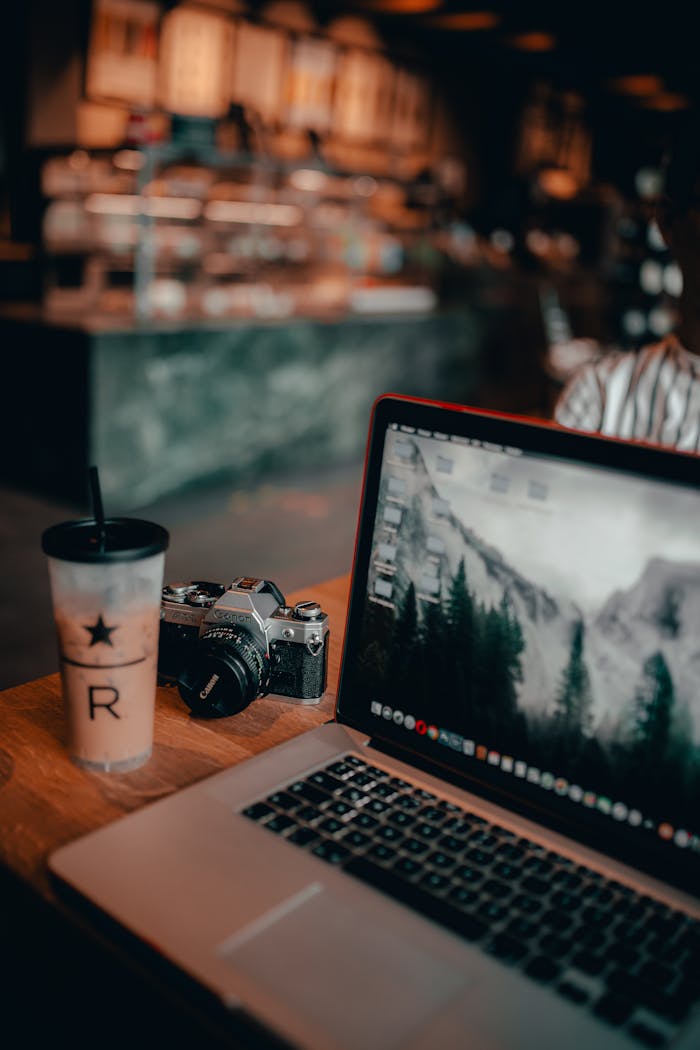 From above of plastic glass of cold coffee placed on table with camera and modern laptop on blurred cafe background